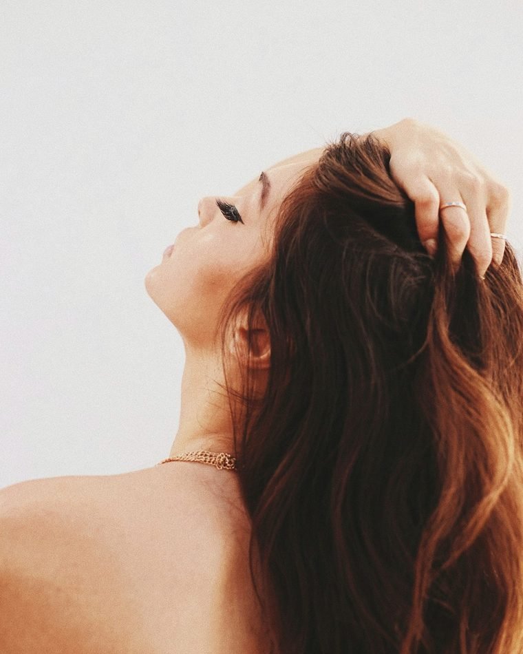 Mulher passando a mão pelo couro cabeludo, cabelo com aspecto saudável
